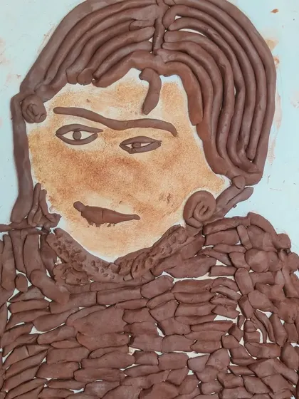 A child's self portrait created using clay on a flat surface. This clay painting and sculpting technique allows for a different kind of detail and expression, showing how they see themselves.