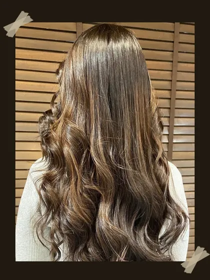 A close-up of long, healthy hair with a rich brown balayage. The soft curls at the ends add volume and showcase the multi-dimensional color.