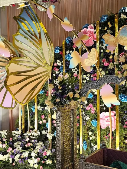 This angle focuses on the beautifully decorated cradle, surrounded by a garden of flowers and fluttering butterflies, making it the perfect centerpiece for a naming ceremony.