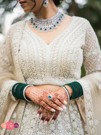 A detail shot of the bride Aishwarya's hands, showcasing her intricate mehndi, green bangles, and stunning white lehenga.