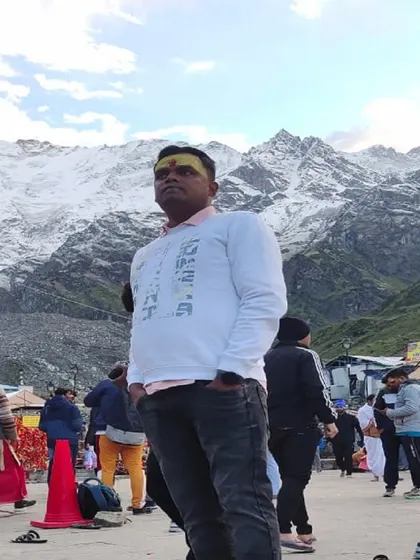 A traveler stands proudly before the Kedarnath temple, with the snow-covered mountains creating a perfect frame. A classic picture capturing the successful completion of a spiritual quest.
