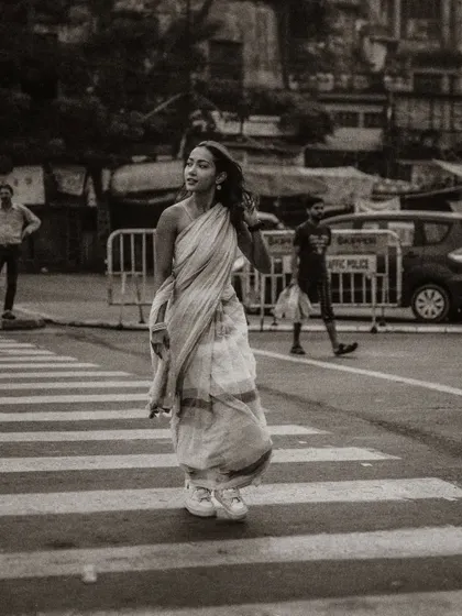 A black and white street photograph of a model crossing the road. The grainy texture and candid moment give this shot a classic, photojournalistic feel.