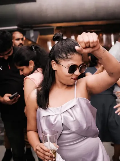 A woman with sunglasses and a drink, dancing with attitude. She owns the dance floor.