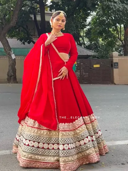 A full-length shot showcasing the complete silhouette of the red velvet bridal lehenga. The long sleeves and coordinated dupatta create a cohesive and elegant look, ideal for a traditional North Indian or fusion wedding ceremony.