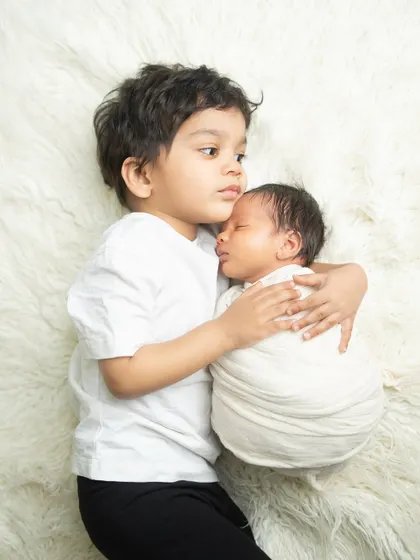 A tender moment between brothers. The older sibling carefully holds his newborn brother, showcasing a bond that will last a lifetime.