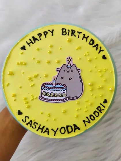 A purr-fectly sweet cat-themed cake. The yellow buttercream is decorated with an edible image of a Pusheen-style cat enjoying its own birthday cake.