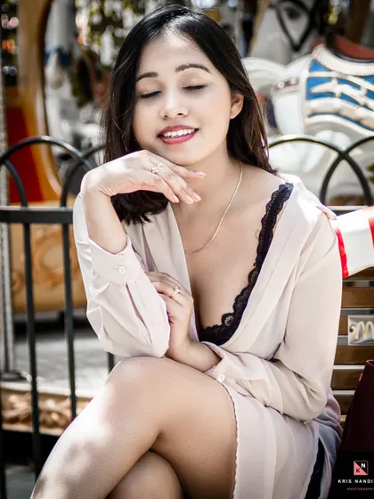 A sweet and serene outdoor portrait taken near a carousel. The model's gentle smile and the soft focus background create a dreamy and romantic atmosphere.