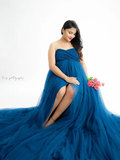 A stunning portrait in a deep blue tulle gown. The mom-to-be is seated, the voluminous dress creating a beautiful sea of blue around her.