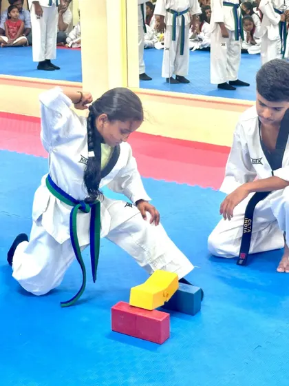 A young girl shows her power and focus by breaking boards during her belt test, a key part of demonstrating proficiency.