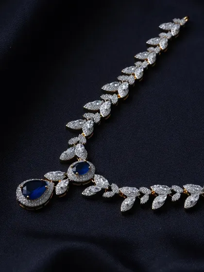This modern necklace features marquise-cut American Diamonds forming a delicate vine pattern. The design culminates in a large, pear-shaped sapphire-blue stone, creating a dramatic and elegant effect.