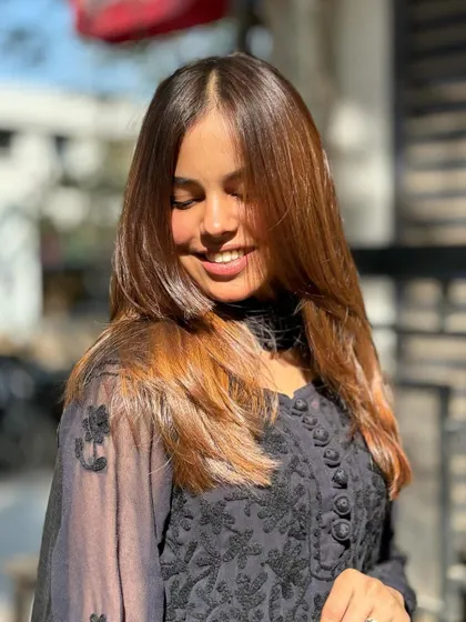 The sunlight catches the warm, golden-brown tones in her hair beautifully. This is the result of a carefully applied color that looks natural and radiant.