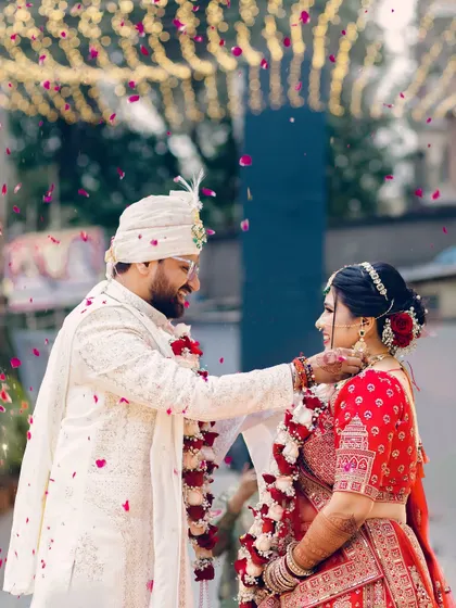 A tender moment during the Varmala ceremony, as the groom gently adjusts the garland for his bride amidst a shower of petals. It’s these small, caring gestures that tell a big story.