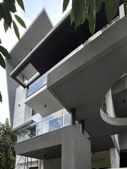 A detail of the 'Madhuram' facade, highlighting the geometric cutouts and the relationship between solid concrete forms and transparent glass railings.