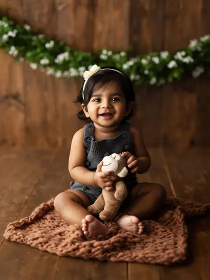 A happy little sitter with her favorite toy monkey. The rustic backdrop and soft rug create a cozy and safe space for her to play and be herself.