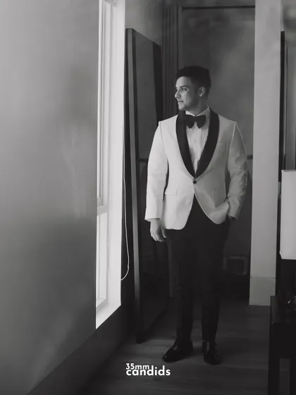 A black and white portrait of the groom, Rohan, looking sharp in his tuxedo. The moody lighting adds a touch of classic elegance.