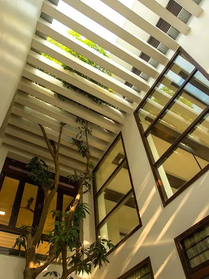 An upward view of the double-height courtyard, showing the slatted pergola ceiling that allows sunlight to filter through, creating beautiful light patterns.