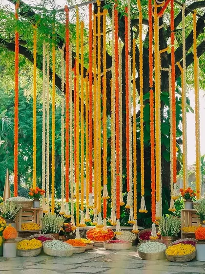 A beautiful backdrop for a Haldi or Mehendi ceremony, created with hanging strings of colorful flowers.