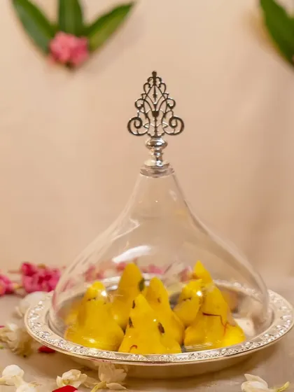 Bappa's favorite treat, modaks, presented in a silver serving dish with a glass cloche. This elegant presentation makes the offering to Lord Ganesha even more special and visually delightful.