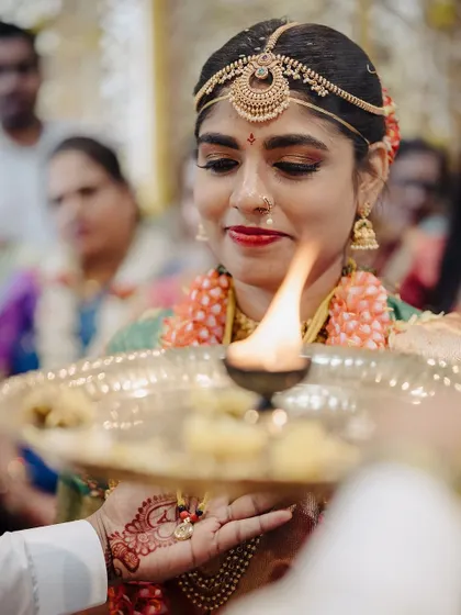 The bride participates in the Aarti ceremony, her face illuminated by the sacred flame. This close up shot captures her serene expression and the spiritual significance of the ritual.