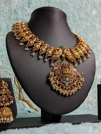 This peacock-inspired antique necklace features a Lakshmi pendant and is perfect for styling with a half saree or a traditional silk saree for a festive occasion.