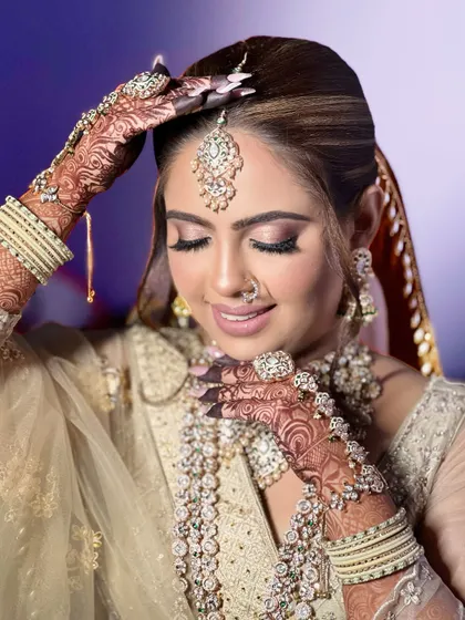 A close-up of a bride in a beautiful beige-gold outfit. The heavy, layered Polki and diamond jewellery set, complete with a large hathphool, creates a look of pure luxury.