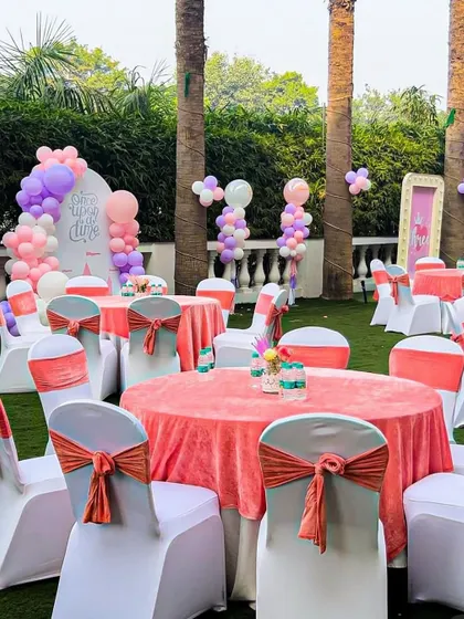 Guest tables at the princess party, decorated with pink tablecloths and coral chair sashes. The balloon decorations in the background tie the whole look together.