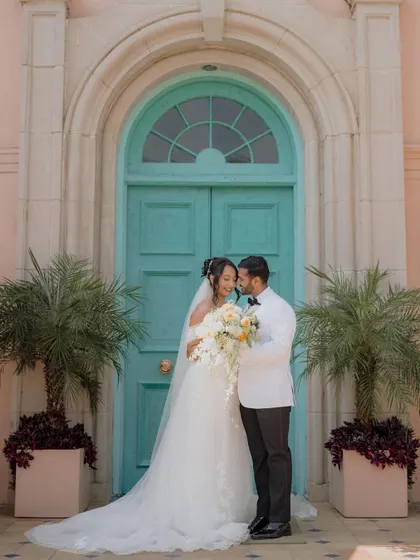 A beautiful portrait of the bride and groom from a Christian wedding, posing in front of a charming turquoise door that adds a pop of color to the scene.