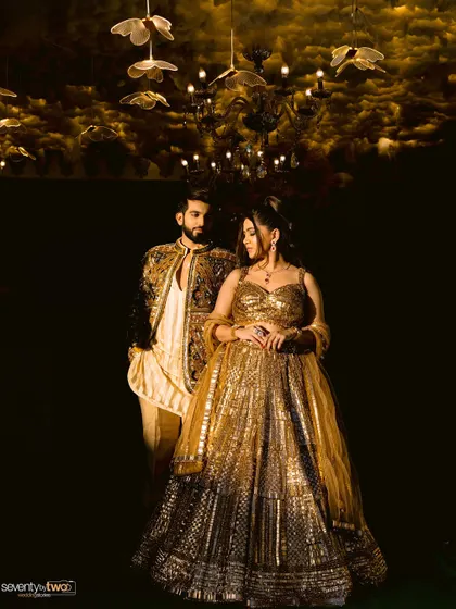 A dramatic, low-light portrait of the couple under a chandelier, their golden outfits shining in the dark.