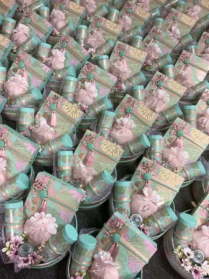 A stunning display of wedding favors ready for dispatch. The pastel color palette of pink and sea-green, combined with delicate floral and tassel details, creates a cohesive and beautiful theme.