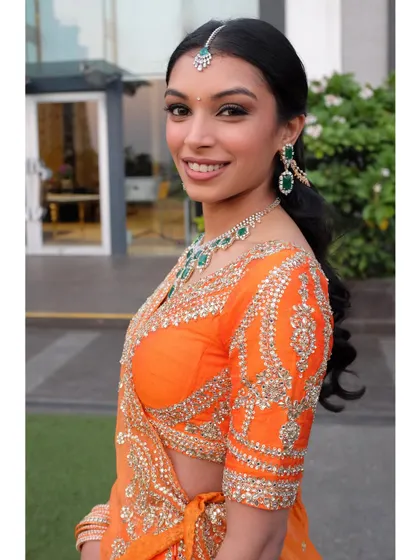 A close-up portrait showing her flawless makeup. I used a winged liner and a warm, peachy-nude lip to complement her orange lehenga and emerald jewelry.