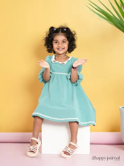 A happy girl in a mint green dress sits against a bright yellow background. The cheerful colors match her vibrant personality perfectly.