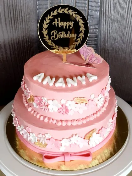 A pretty two-tier pink floral cake with a butterfly accent. The tiers are decorated with delicate fondant flowers and a pearl border.
