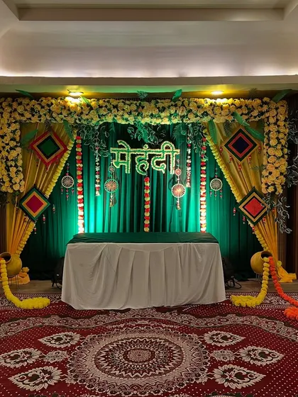 A classic Mehendi setup with a green and yellow backdrop, floral arrangements, and traditional hangings, perfect for creating a festive vibe.
