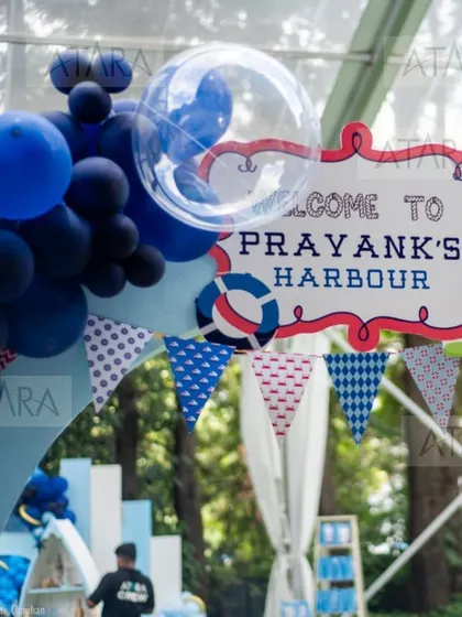 A close-up of the welcome sign and balloon arch for "Prayank's Harbour." The clear bubble balloon and navy blue color scheme are perfect for a nautical theme.