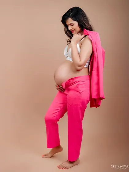 A confident and modern maternity portrait. The mom-to-be wears a hot pink suit jacket draped over her shoulder, showcasing her bump with style.