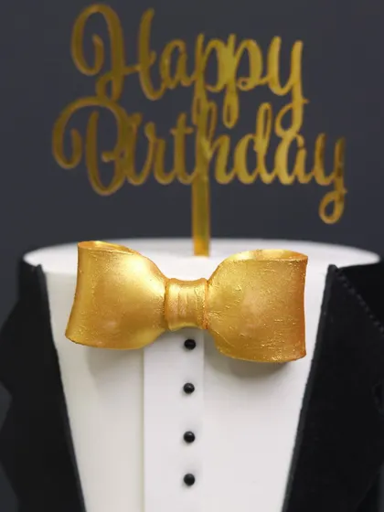 A close-up of the sharp details on the Gentlemen Cake, featuring a crisp tuxedo shirt and a perfectly sculpted golden bow tie.