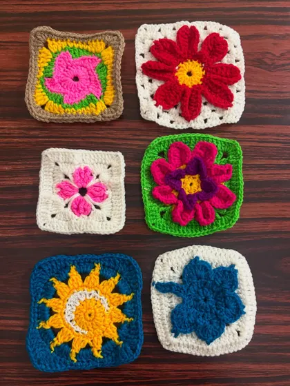 A collection of six colorful granny square coasters, each with a unique floral or sun-inspired design in the center.
