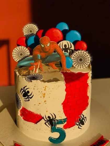 A Spiderman-themed cake for a 5th birthday party. This design features edible webs, city details, and a Spiderman topper, bringing the superhero action to the celebration.