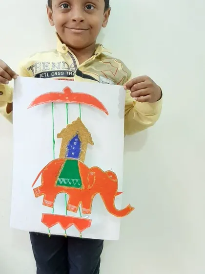 A child proudly holds up his artwork of a decorated elephant, created for the Dusshera festival. These projects allow children to learn about cultural symbols through their own creative work.