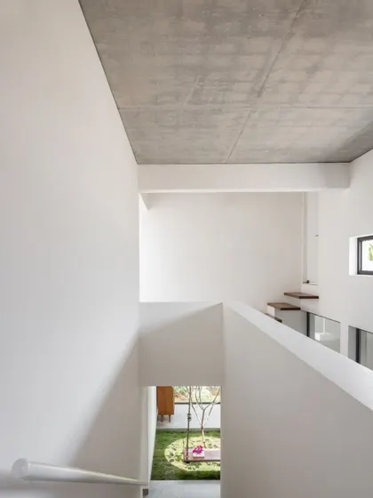 Looking down from the first floor into the central courtyard, this view reveals the home's vertical connection. The exposed concrete ceiling and crisp white walls are part of our simple, durable, and cost-effective material palette.