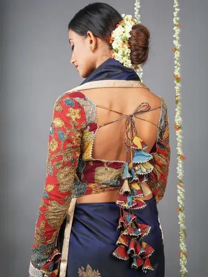 This stunning blouse features a full-back opening with an elaborate tassel tie-up. The sleeves and body are covered in a rich, red and yellow Kalamkari print.