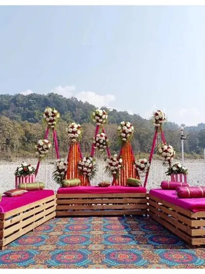 A rustic and colorful Mehendi stage setup by the river, using wooden pallet sofas and traditional Indian prints.