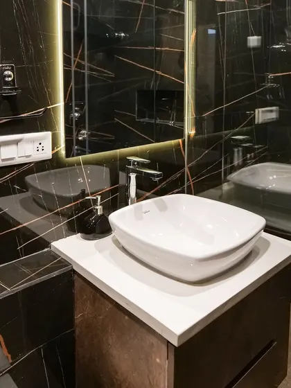 This bathroom from a completed project features dramatic black marble with gold veining, a modern vessel sink, and backlit mirror, creating a luxurious and moody retreat.