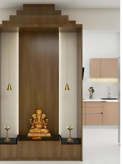 A freestanding pooja unit designed to look like a small temple. The wooden structure with backlighting creates a divine glow, and the unit is placed to be visible from the adjacent kitchen.