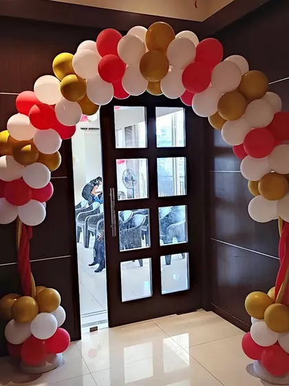 A simple yet elegant balloon arch at the entrance of a naming ceremony event, welcoming guests with a classic red, white, and gold color scheme.