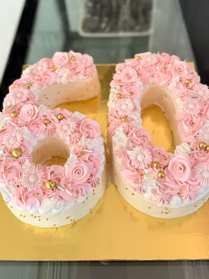 A stunning number cake for a 60th birthday celebration. The "60" is formed from soft sponge and decorated with intricate pink and white floral piping and delicate gold bead accents.