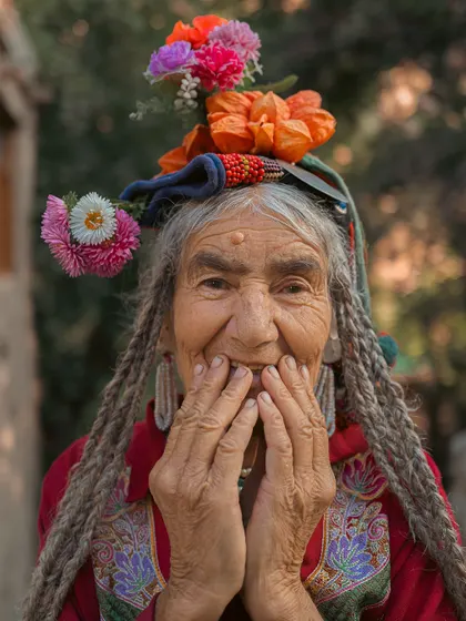 A portrait of a Brokpa woman in Ladakh, her face full of joy and life. Her traditional floral headdress and intricate clothing tell the story of her ancient and vibrant culture.