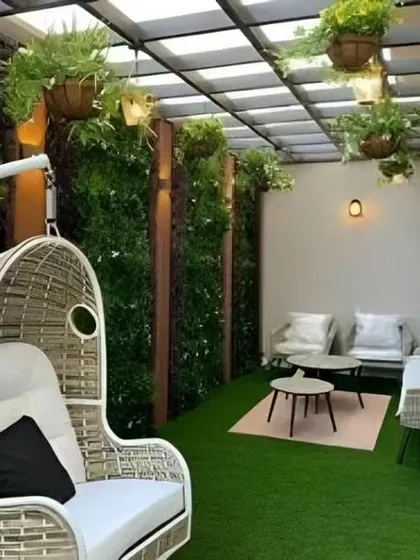 This covered patio is a cozy retreat, featuring a comfortable swing chair and vertical gardens. The artificial grass and hanging plants create a lush, green environment protected from the elements.