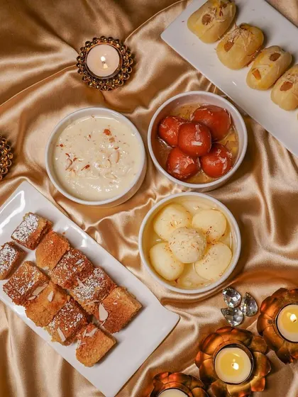 A festive tabletop arrangement of Indian sweets, including gulab jamun and rasgulla, styled with golden fabric and lit diyas. This is an example of my food photography for seasonal campaigns and brand promotions.