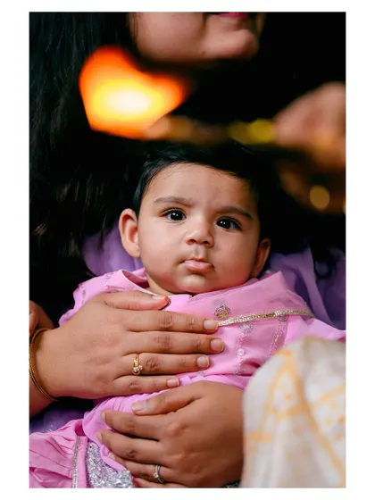 A beautiful baby portrait taken during a traditional ceremony. The soft lighting from the lamp adds a warm glow to this peaceful moment.